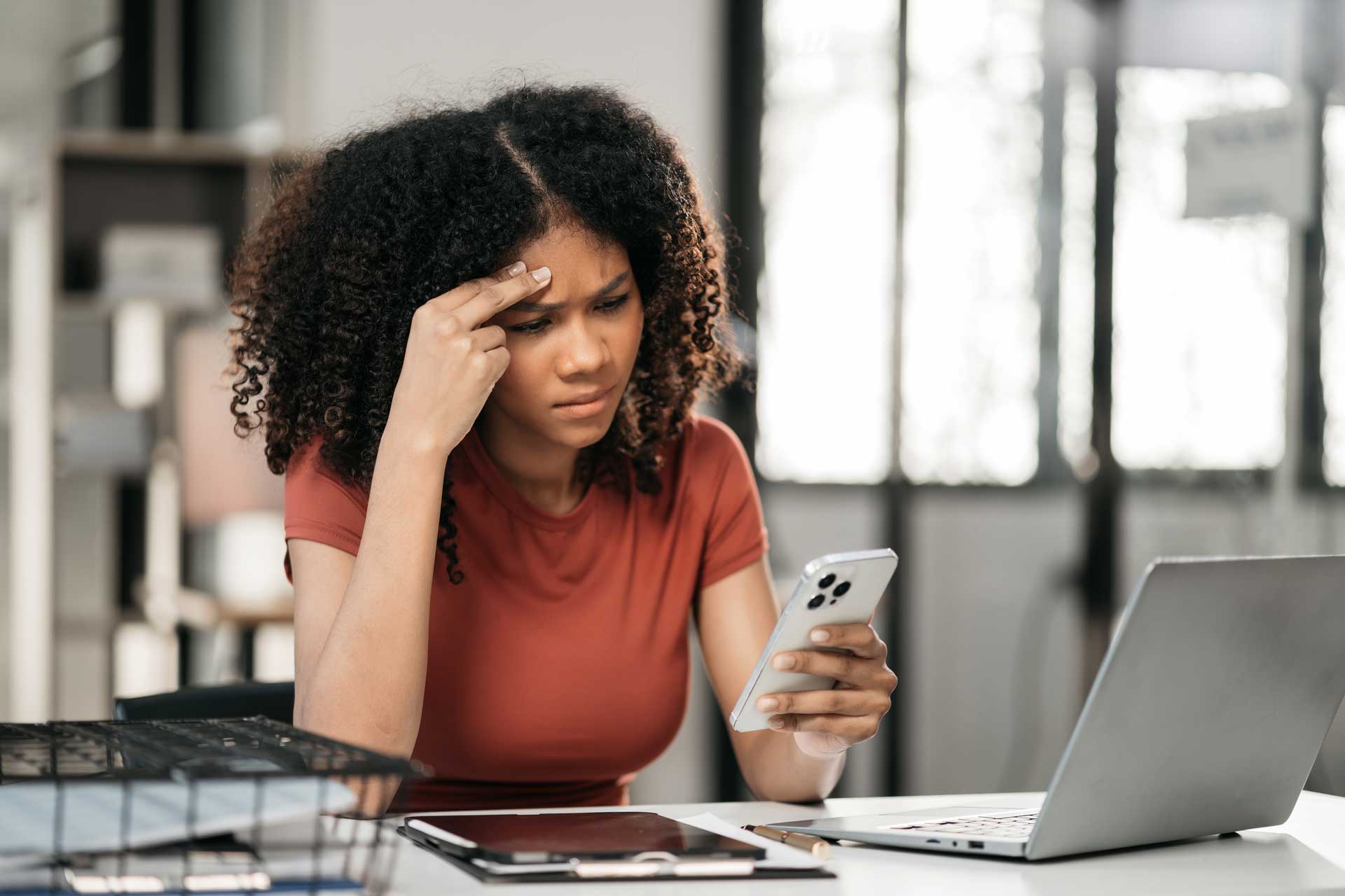 frustrated woman on phone and laptop with hand on foredhead